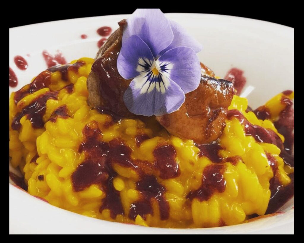 Un risotto allo zafferano cremoso decorato con una violetta.